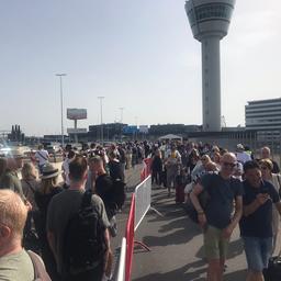 Reizigers wachten buiten in hitte voor Schiphol, medewerkers delen water uit